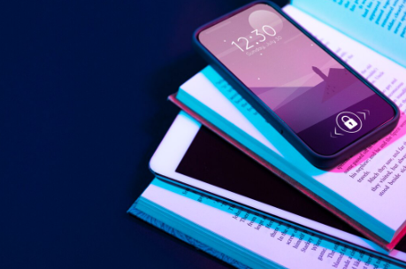 A smartphone and a tablet rest on an open book. The screens are illuminated with a purple and blue light, and the phone shows the time and date.