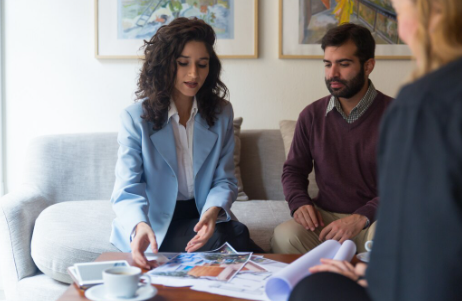 A professional woman in a blue blazer and two other people, a man and a woman, are seated on a couch, discussing documents on a coffee table.