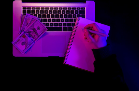 A hand holds a pen to sign a "Loan Application Form" on a clipboard with a pink header, on a wooden desk.