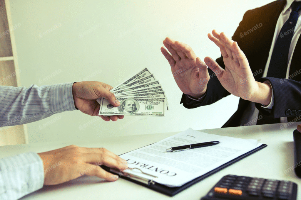 "Businessman refusing a bribe as another person offers a stack of US dollar bills across a desk with a contract and pen."