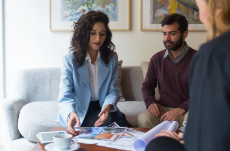 "Group of people having a business meeting at a table with documents and coffee cups, as a woman in a blue blazer explains something."