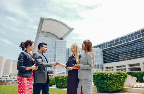 "Group of business professionals standing outside a modern office building, with two of them shaking hands."