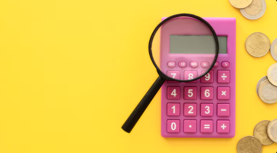 "Pink calculator with a magnifying glass on top and scattered coins on a yellow background."