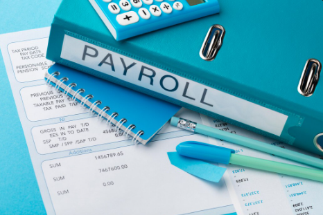 "Close-up of payroll documents with a blue binder, notebook, calculator, and office supplies on a desk."