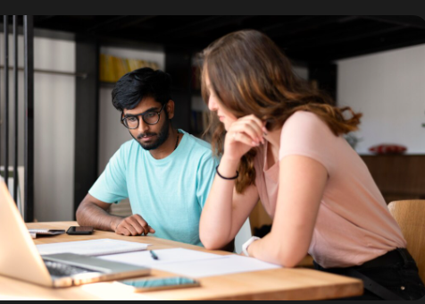 "Two colleagues working together at a desk, looking at a laptop and documents."