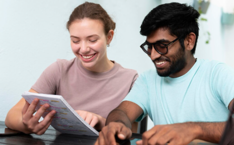 "Smiling young woman and man sitting together, looking at notes in a notebook."